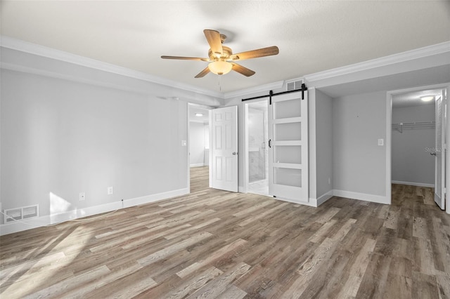 unfurnished bedroom with ceiling fan, a barn door, crown molding, a walk in closet, and a closet