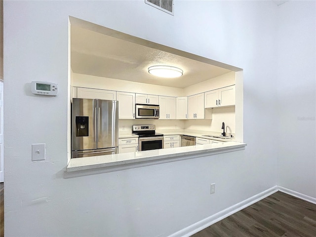 kitchen featuring kitchen peninsula, appliances with stainless steel finishes, dark hardwood / wood-style flooring, sink, and white cabinets