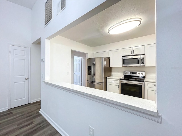 kitchen with white cabinetry, light stone countertops, dark wood-type flooring, a textured ceiling, and appliances with stainless steel finishes