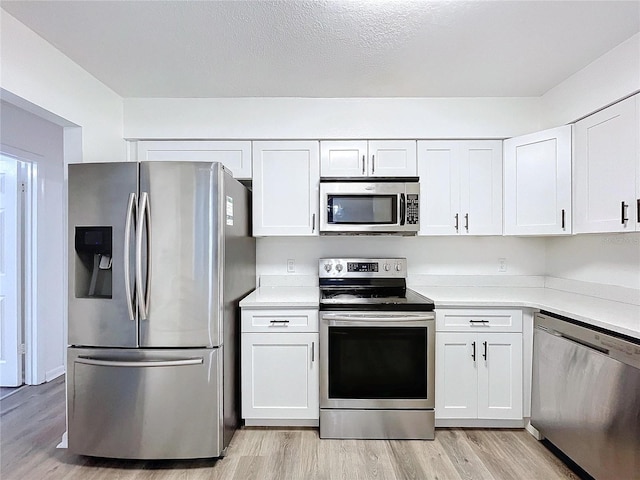 kitchen with white cabinets, a textured ceiling, stainless steel appliances, and light hardwood / wood-style flooring