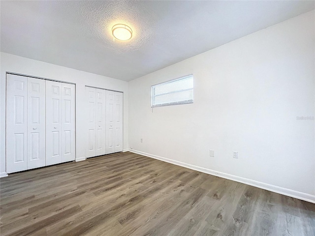 unfurnished bedroom featuring two closets, dark hardwood / wood-style floors, and a textured ceiling