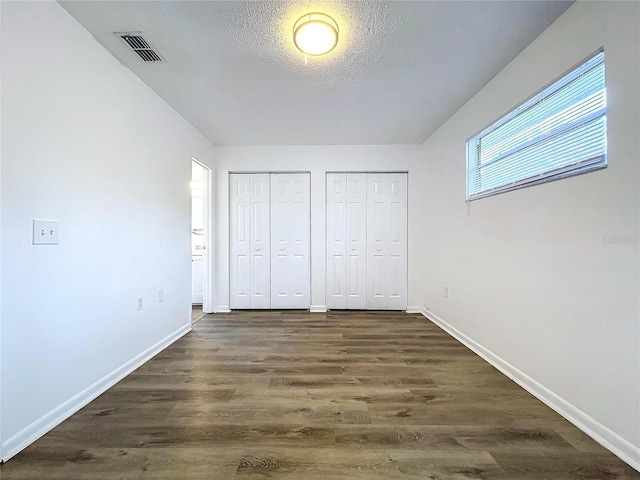 unfurnished bedroom with two closets, a textured ceiling, and dark hardwood / wood-style floors