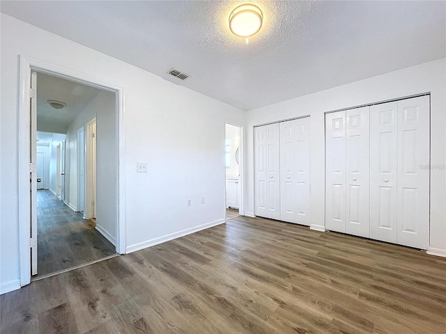 unfurnished bedroom with dark hardwood / wood-style floors, a textured ceiling, and two closets