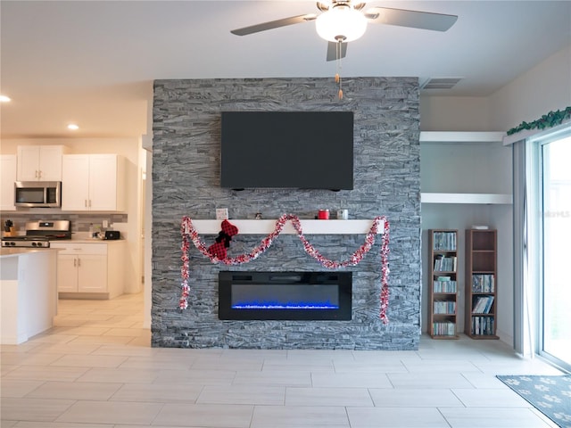 living room with built in shelves, a stone fireplace, ceiling fan, and a healthy amount of sunlight