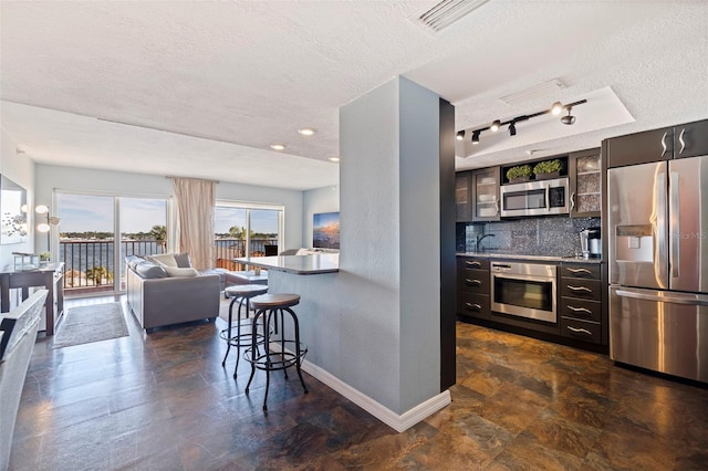 kitchen featuring appliances with stainless steel finishes, backsplash, track lighting, a kitchen breakfast bar, and a textured ceiling