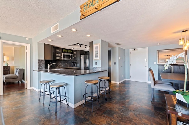 kitchen featuring kitchen peninsula, appliances with stainless steel finishes, a kitchen bar, tasteful backsplash, and a textured ceiling