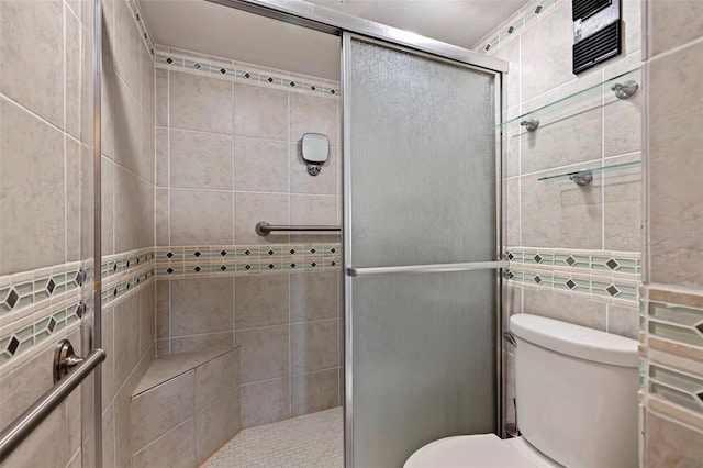 bathroom with toilet, a shower with shower door, and tile walls