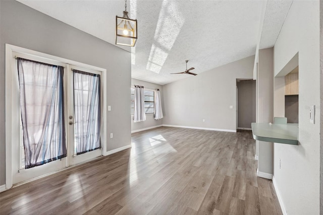 unfurnished living room featuring ceiling fan, french doors, a textured ceiling, vaulted ceiling, and light wood-type flooring