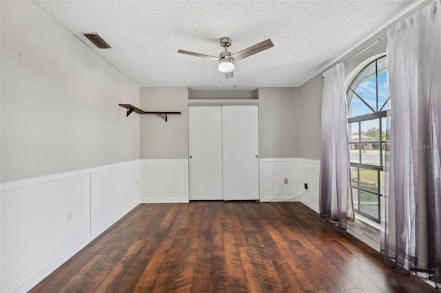 empty room featuring a textured ceiling, ceiling fan, dark wood-type flooring, and a wealth of natural light