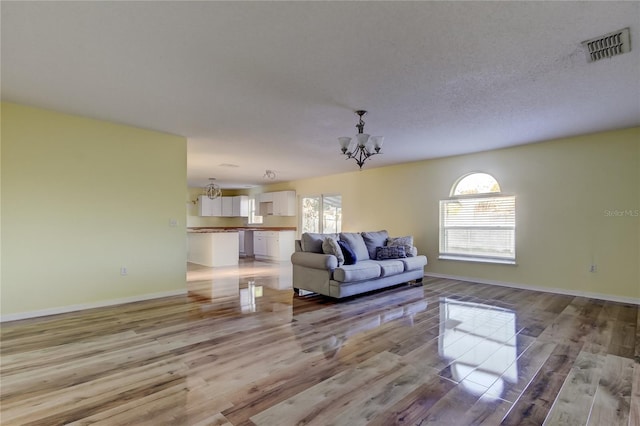 living room with light wood-type flooring, a textured ceiling, and a notable chandelier