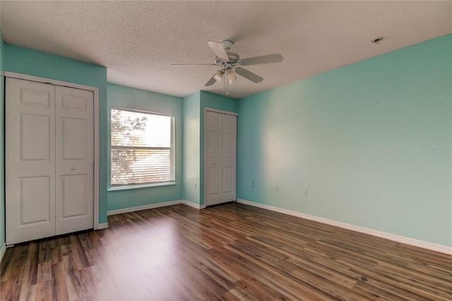 unfurnished bedroom featuring two closets, ceiling fan, dark wood-type flooring, and a textured ceiling