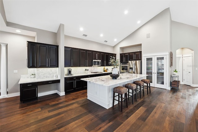 kitchen with a breakfast bar, dark hardwood / wood-style floors, a kitchen island, stainless steel appliances, and decorative backsplash