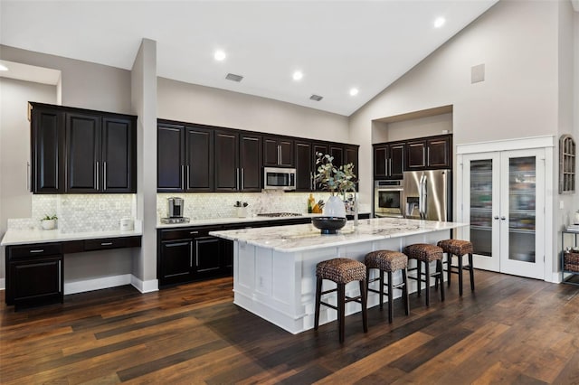 kitchen featuring dark wood-type flooring, a breakfast bar, stainless steel appliances, light stone countertops, and an island with sink