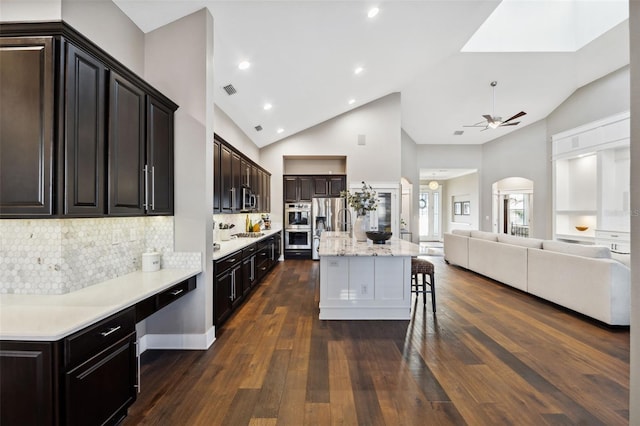 kitchen with high vaulted ceiling, dark hardwood / wood-style floors, a center island, a kitchen bar, and decorative backsplash