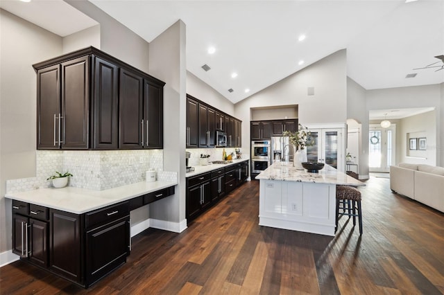 kitchen with dark wood-type flooring, appliances with stainless steel finishes, a kitchen breakfast bar, a center island, and decorative backsplash