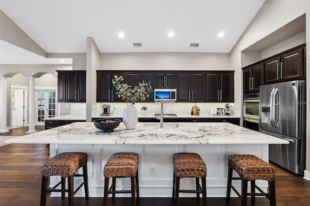 kitchen featuring a breakfast bar, stainless steel appliances, an island with sink, dark hardwood / wood-style flooring, and ornate columns