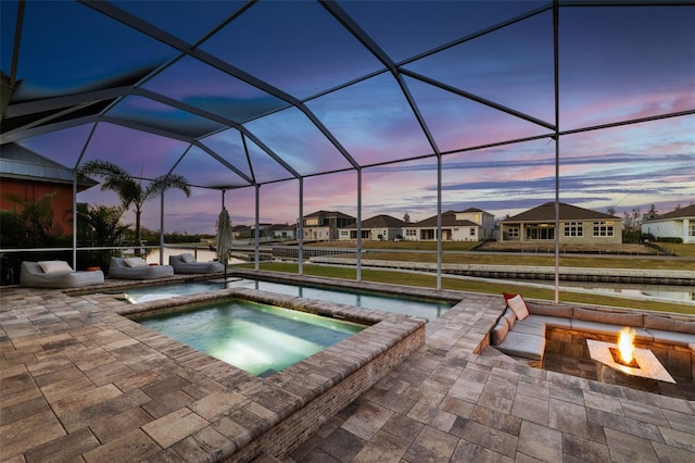 pool at dusk with an in ground hot tub, an outdoor fire pit, a lanai, and a patio area