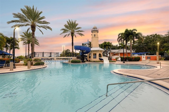 pool at dusk featuring a water slide and a patio area