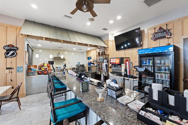 kitchen with a breakfast bar, refrigerator, hanging light fixtures, ceiling fan, and dark stone counters