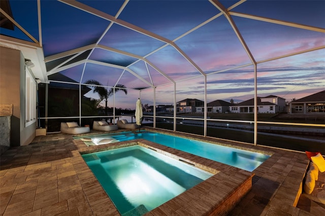 pool at dusk with a patio area, an outdoor pool, an in ground hot tub, and a lanai