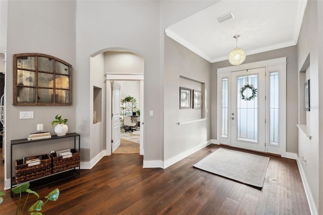 foyer featuring visible vents, ornamental molding, dark wood finished floors, arched walkways, and baseboards