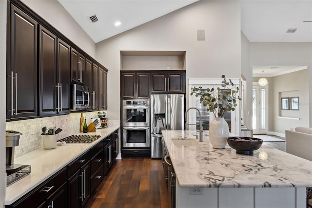 kitchen featuring visible vents, lofted ceiling, an island with sink, a sink, and appliances with stainless steel finishes