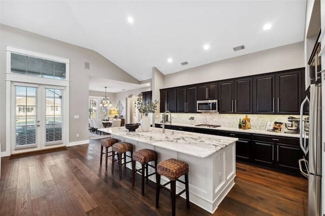 kitchen with visible vents, dark wood-type flooring, a kitchen breakfast bar, tasteful backsplash, and appliances with stainless steel finishes