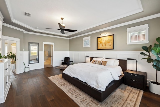 bedroom with visible vents, a tray ceiling, ornamental molding, wainscoting, and dark wood-style flooring