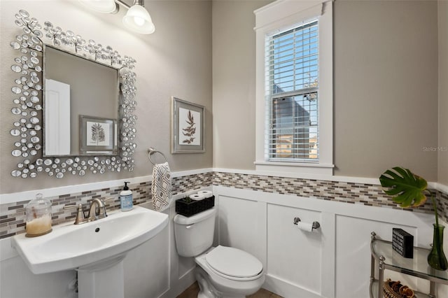 half bathroom with toilet, a wainscoted wall, and a sink