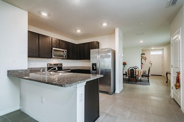 kitchen with sink, appliances with stainless steel finishes, dark brown cabinetry, kitchen peninsula, and dark stone counters