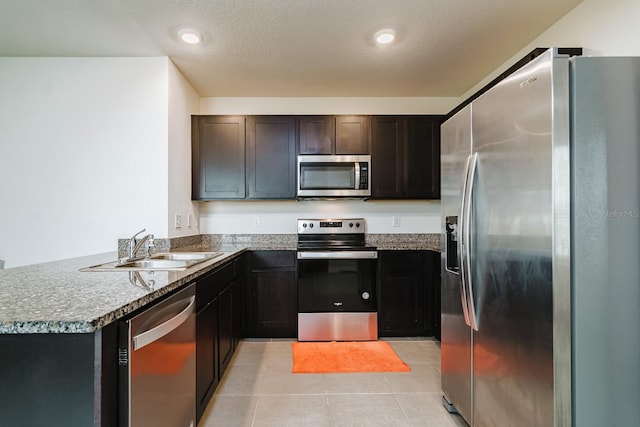 kitchen featuring sink, a textured ceiling, light tile patterned floors, kitchen peninsula, and stainless steel appliances