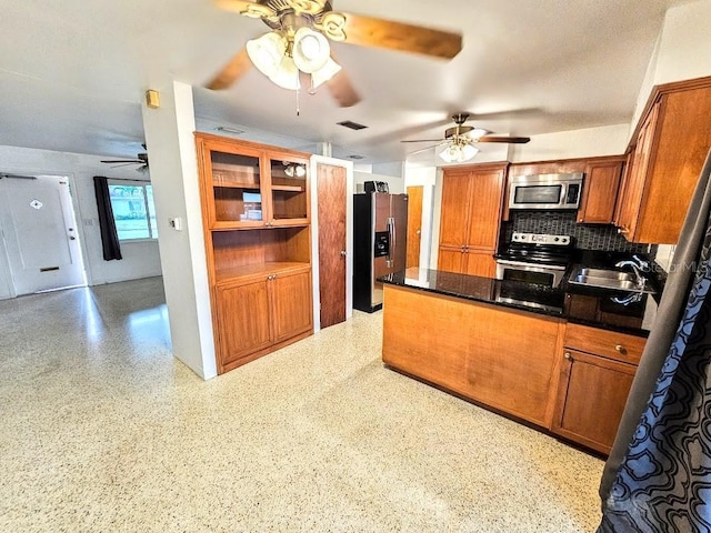 kitchen with sink, decorative backsplash, dark stone countertops, appliances with stainless steel finishes, and kitchen peninsula