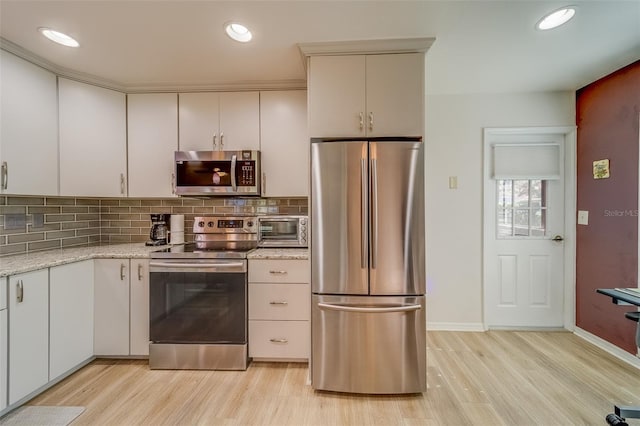 kitchen with light wood-type flooring, backsplash, light stone counters, stainless steel appliances, and white cabinets