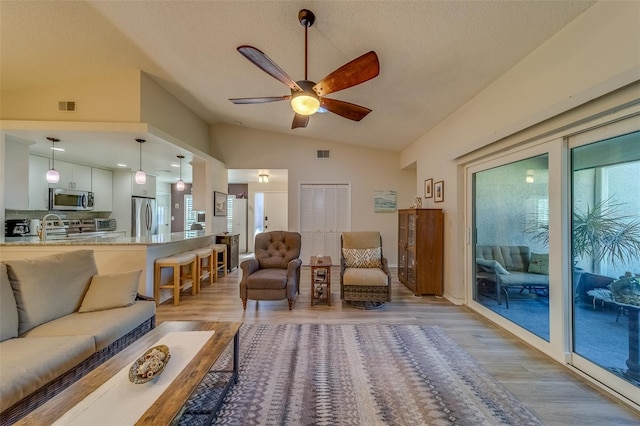 living room featuring ceiling fan, sink, light hardwood / wood-style floors, a textured ceiling, and vaulted ceiling