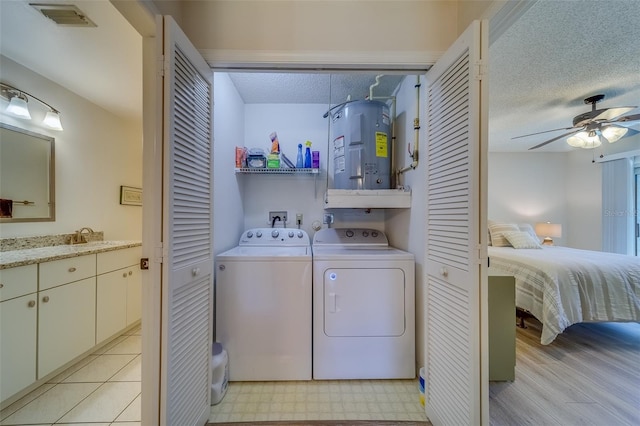 laundry room with ceiling fan, sink, water heater, a textured ceiling, and washer and dryer