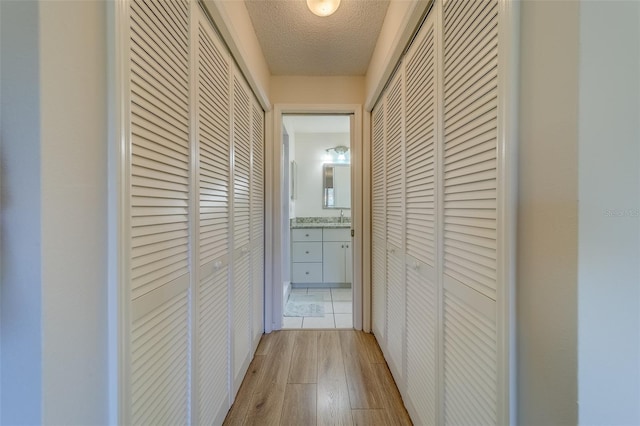 hall with light wood-type flooring and a textured ceiling