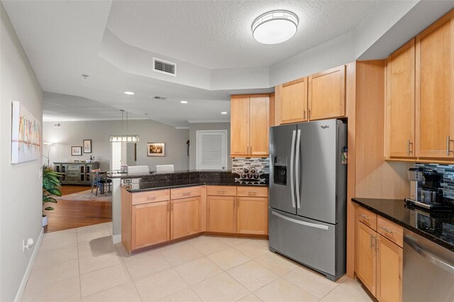 kitchen featuring decorative backsplash, appliances with stainless steel finishes, a textured ceiling, light brown cabinets, and dark stone countertops