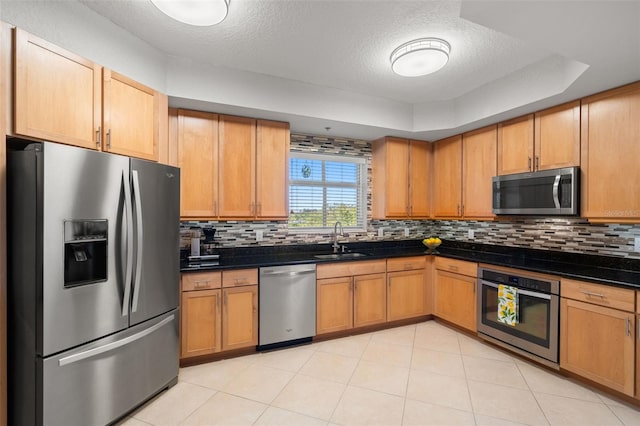 kitchen with appliances with stainless steel finishes, backsplash, a textured ceiling, a tray ceiling, and sink