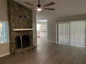 unfurnished living room featuring ceiling fan, a stone fireplace, and wood-type flooring