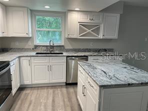 kitchen with white cabinets, sink, light hardwood / wood-style floors, light stone counters, and stainless steel appliances