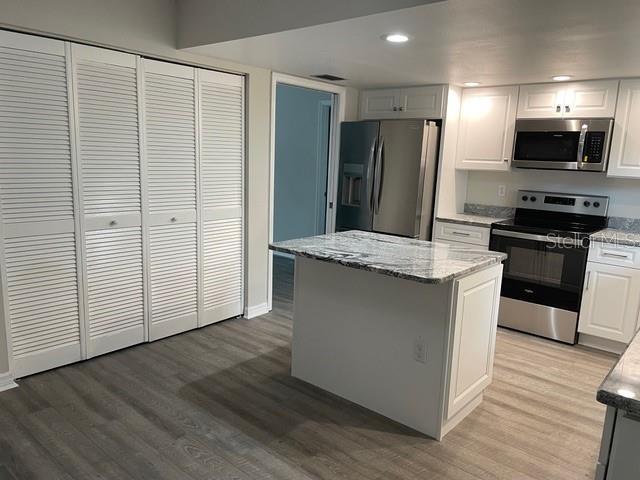 kitchen featuring white cabinets, light stone counters, appliances with stainless steel finishes, a kitchen island, and hardwood / wood-style flooring