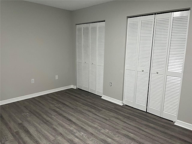 unfurnished bedroom featuring dark wood-type flooring and two closets