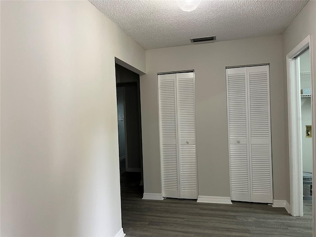 unfurnished bedroom with a textured ceiling, dark wood-type flooring, and multiple closets