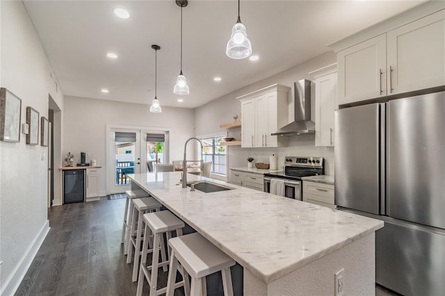 kitchen featuring a center island with sink, white cabinets, sink, wall chimney exhaust hood, and appliances with stainless steel finishes