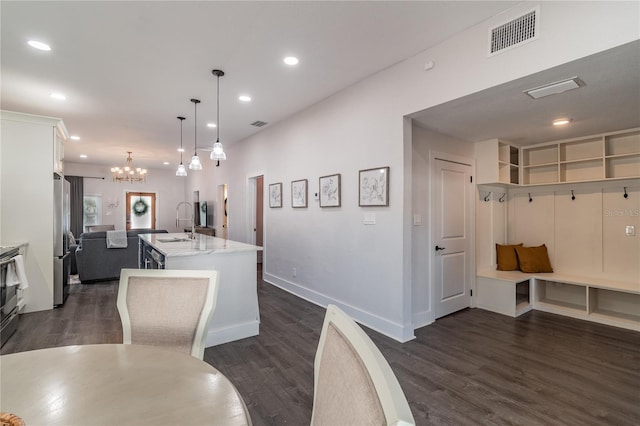 kitchen with a kitchen island with sink, sink, white cabinets, stainless steel refrigerator, and hanging light fixtures