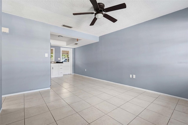 tiled empty room with ceiling fan, a textured ceiling, and a tray ceiling