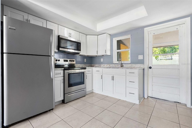 kitchen with sink, white cabinets, light tile patterned floors, a tray ceiling, and stainless steel appliances