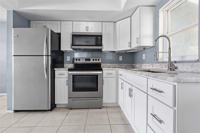 kitchen with sink, white cabinets, light tile patterned floors, and stainless steel appliances