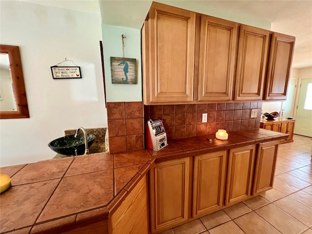 kitchen with light tile patterned floors, tile counters, decorative backsplash, and sink