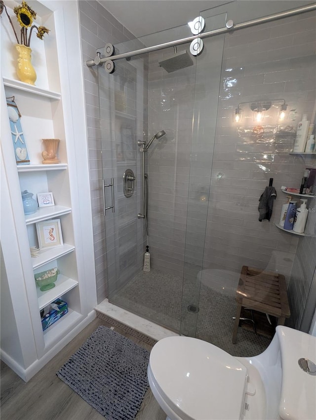 bathroom with wood-type flooring, built in shelves, toilet, and a shower with door